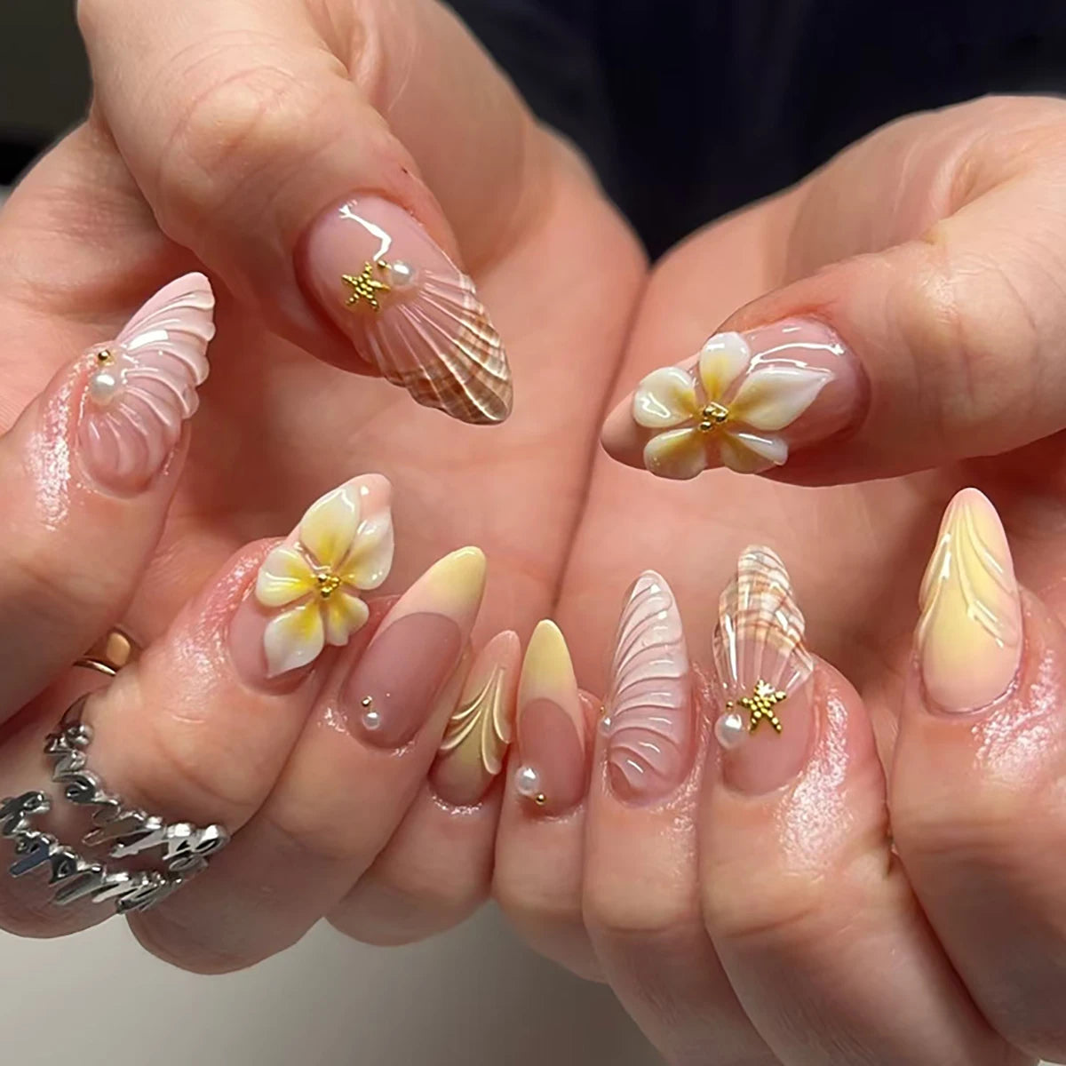 Uñas almendradas hechas a mano con degradado rosa *nude*, decoradas con conchas en 3D, flores de plumeria y perlas. Reutilizables, perfectas para el día a día.