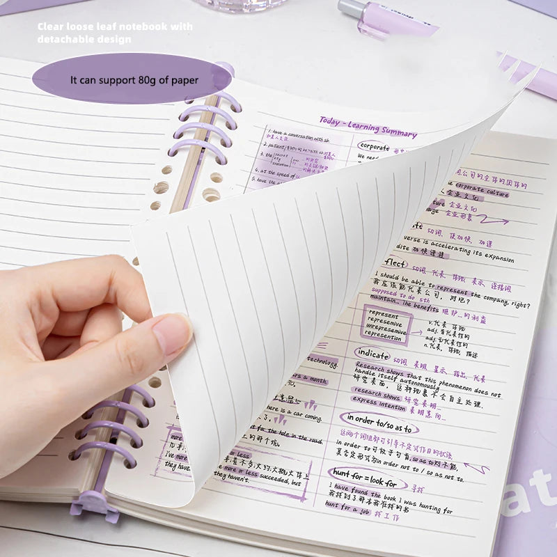 Cuaderno A5 de hojas sueltas (60 hojas/120 páginas) con cubierta de piel sintética flexible y translúcida, anillas desmontables y rayado horizontal.